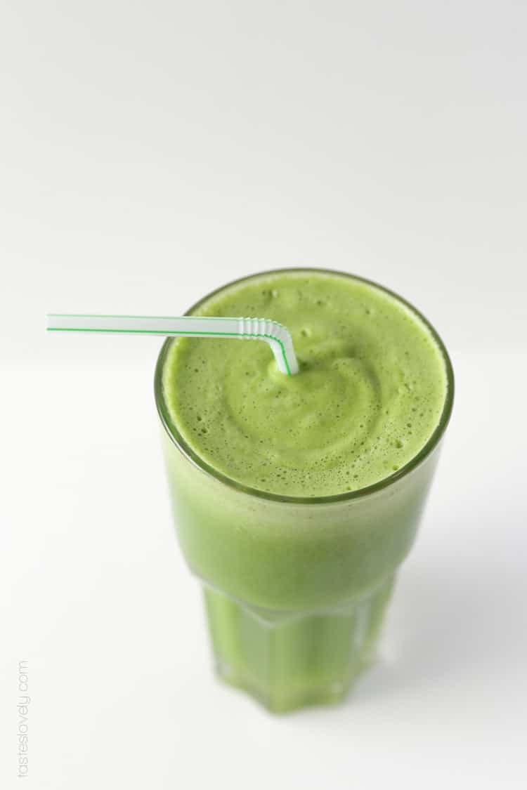 an overhead shot of a green smoothie in a glass with a plastic straw