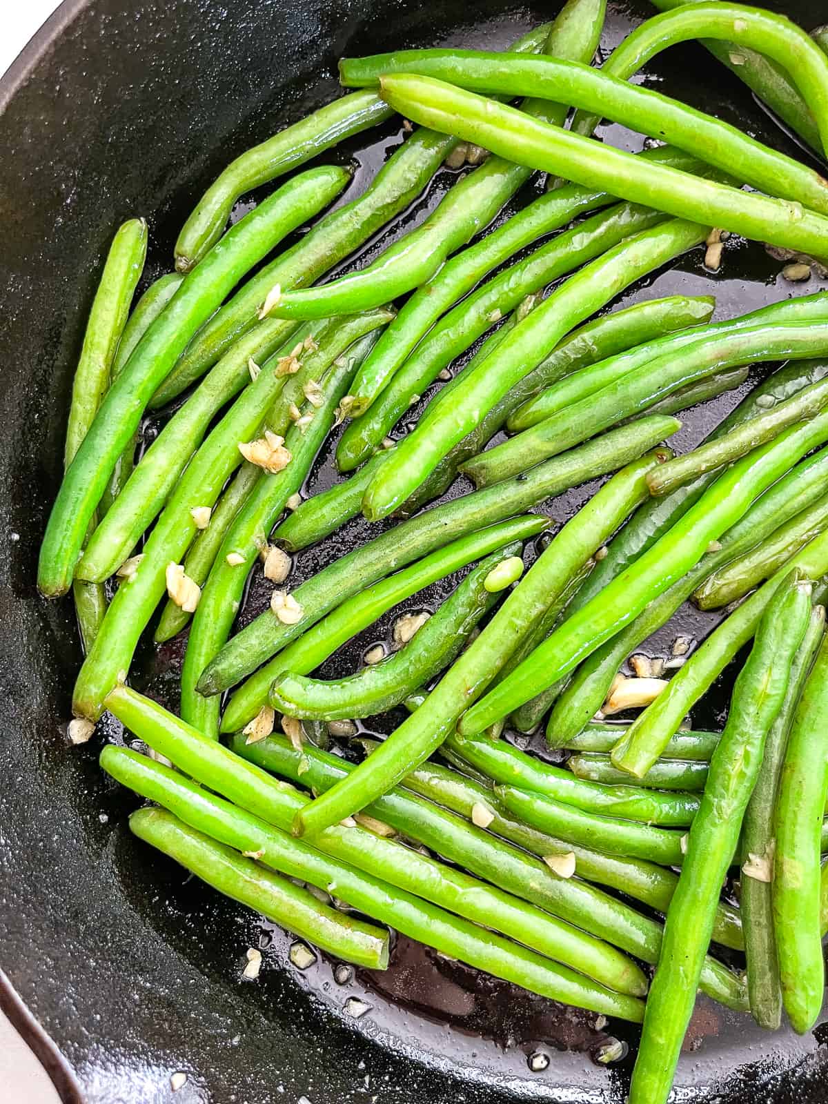 fresh green beans cooking in garlic and butter in a cast iron skillet