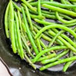 close up of green beans cooking in cast iron skillet with garlic and butter