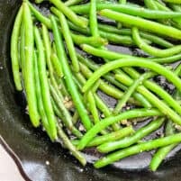 close up of green beans cooking in cast iron skillet with garlic and butter