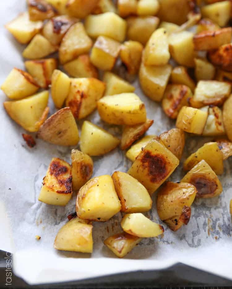 a closeup photo of diced roasted golden potatoes on a lined baking sheet