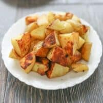 a piled of roasted golden potatoes on a white plate