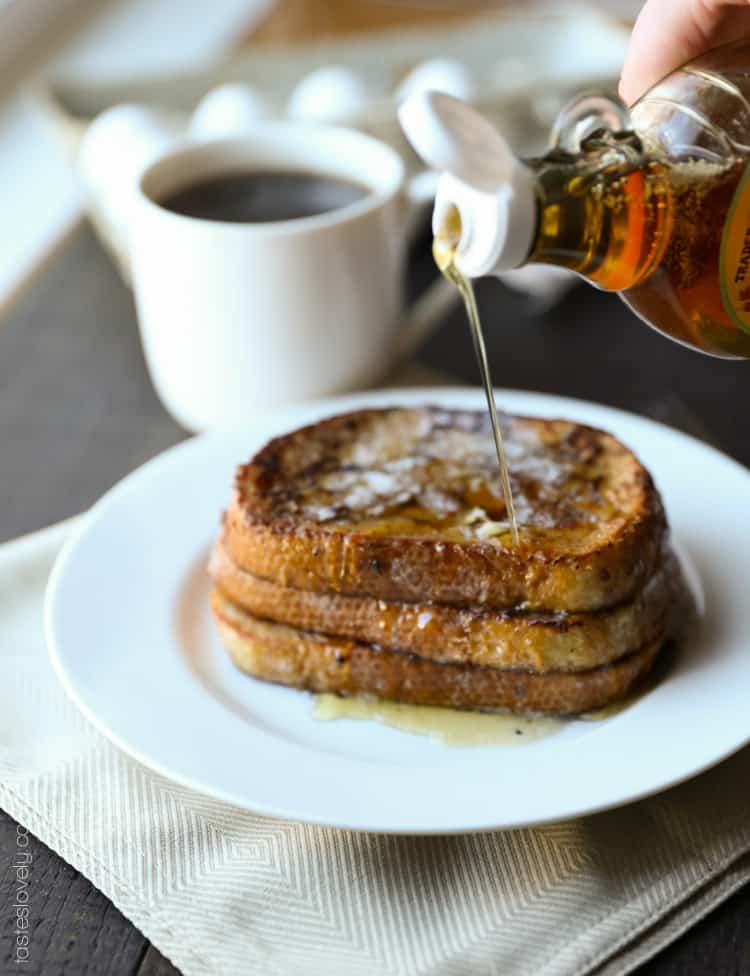 a stack of three sourdough french toast slices on a white plate with maple syrup being poured overtop