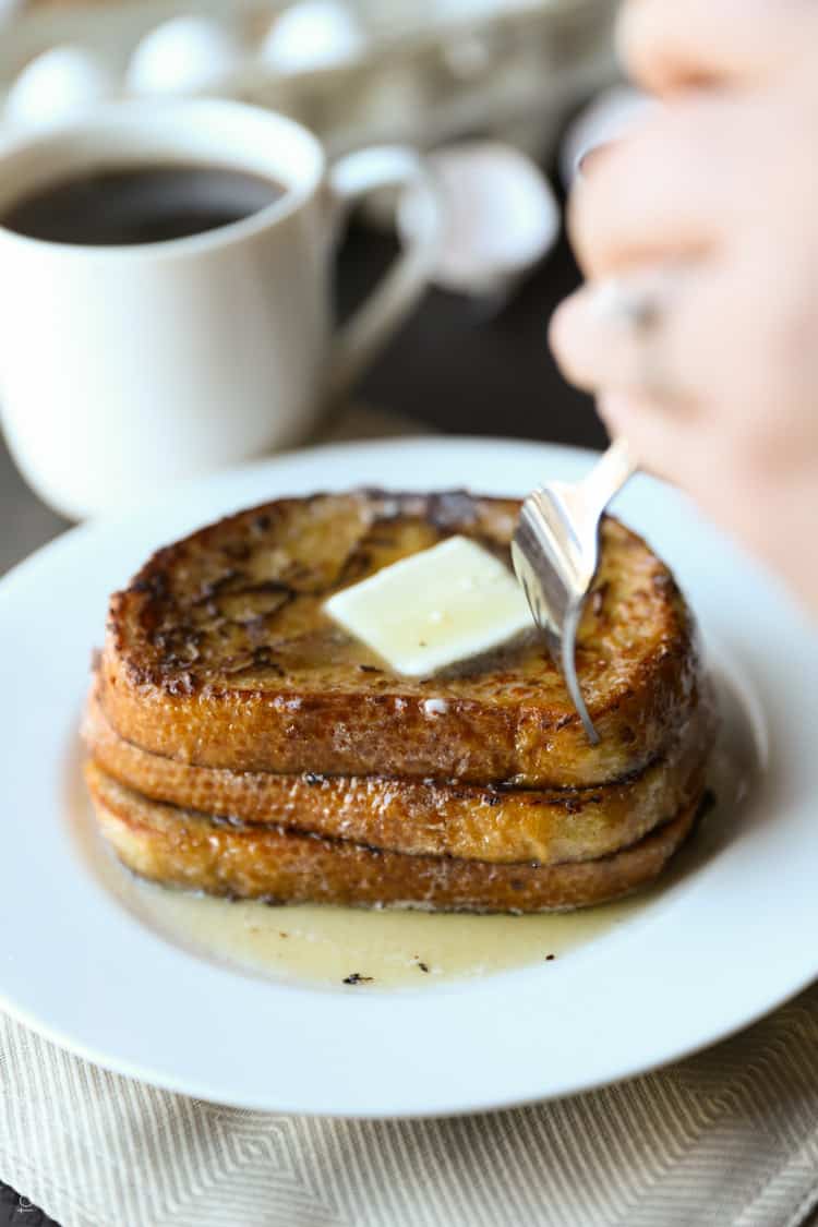 a fork cutting into a stack of three pieces of french toast