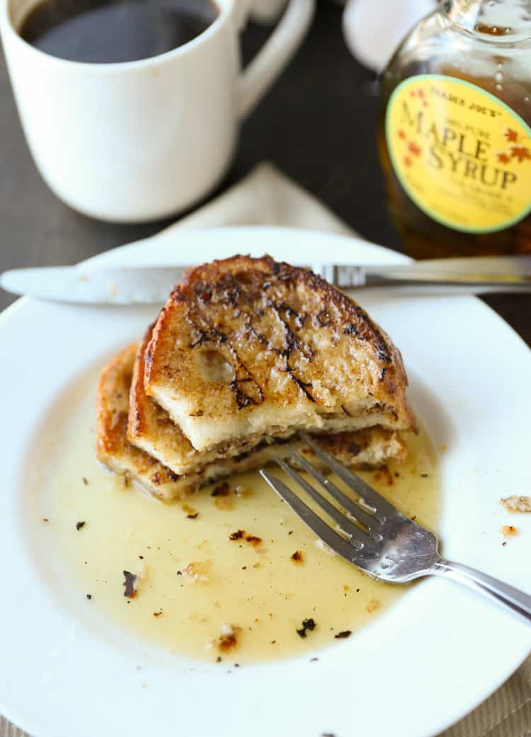 a white plate with a silver fork and a pool of maple syrup in the middle with half eaten french toast