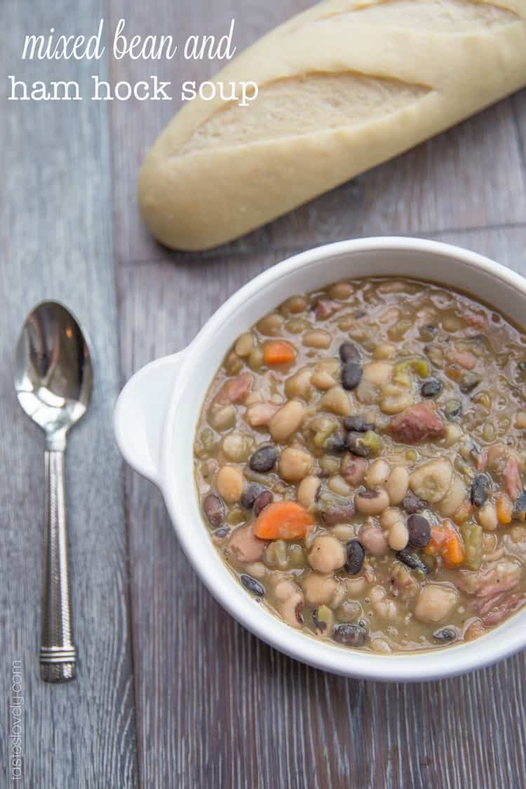 a white bowl filled with bean soup with a silver spoon next to it and a french baguette above it. 