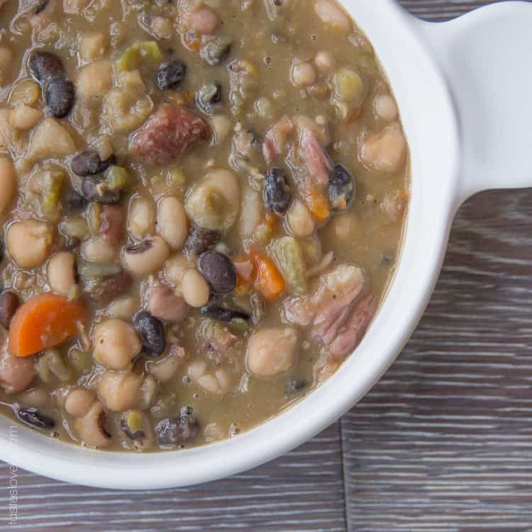 a close up of a white bowl of bean soup with chunks of ham and veggies