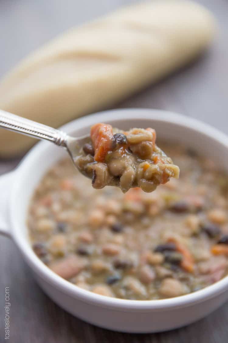 a closeup shot of a silver spoon holding a scoop of bean soup with a white bowl filled with bean soup in the background