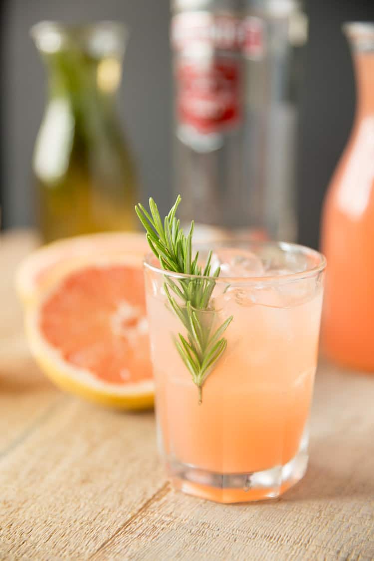 a closeup of a glass filled with vodka and grapefruit juice with a rosemary infused simple syrup