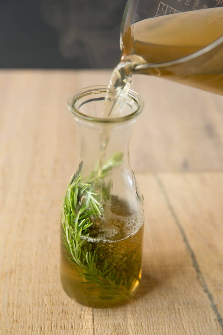 a photo of a measuring glass pouring rosemary simple syrup into a glass jar