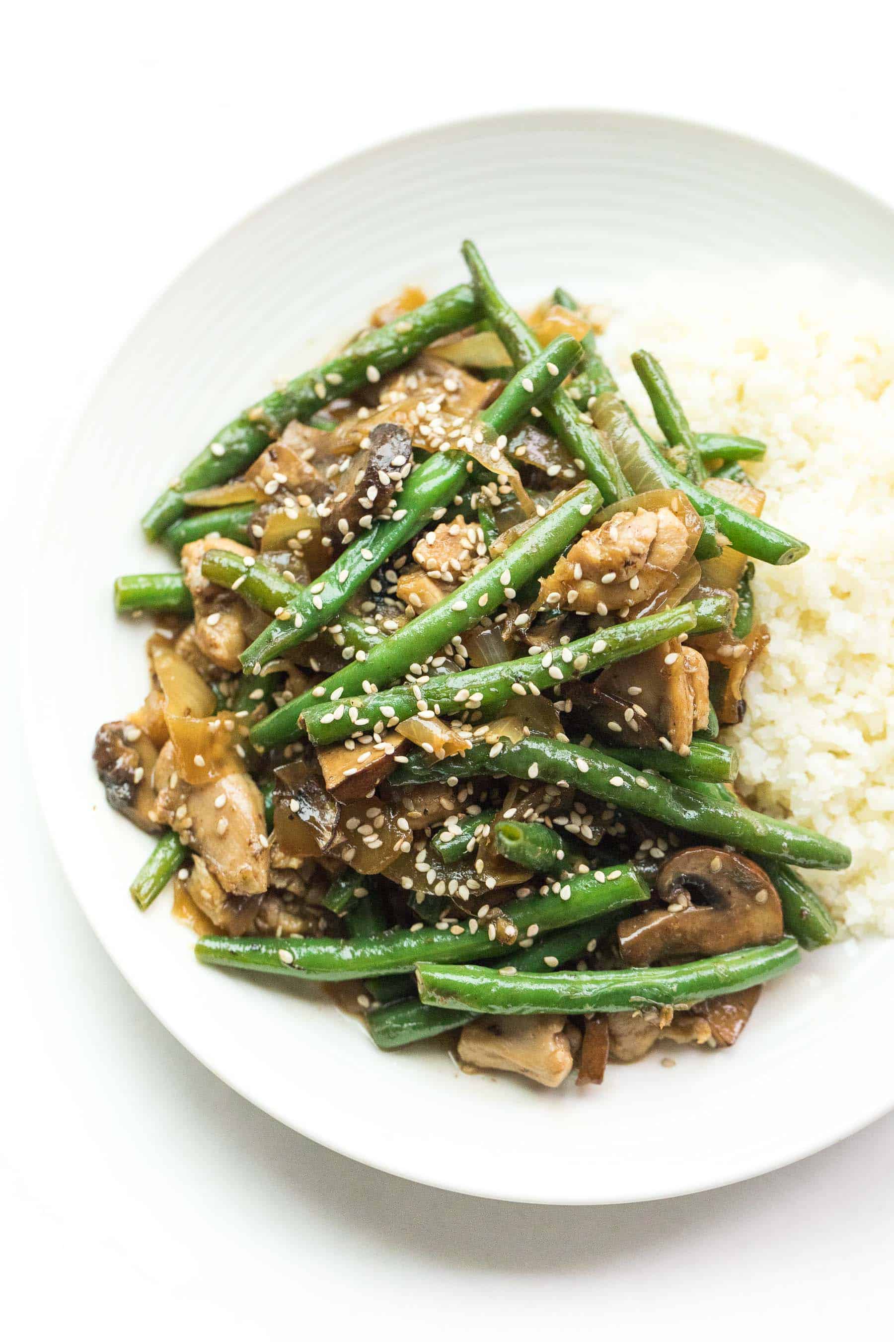 sesame chicken green bean stir fry on a white plate with cauliflower rice