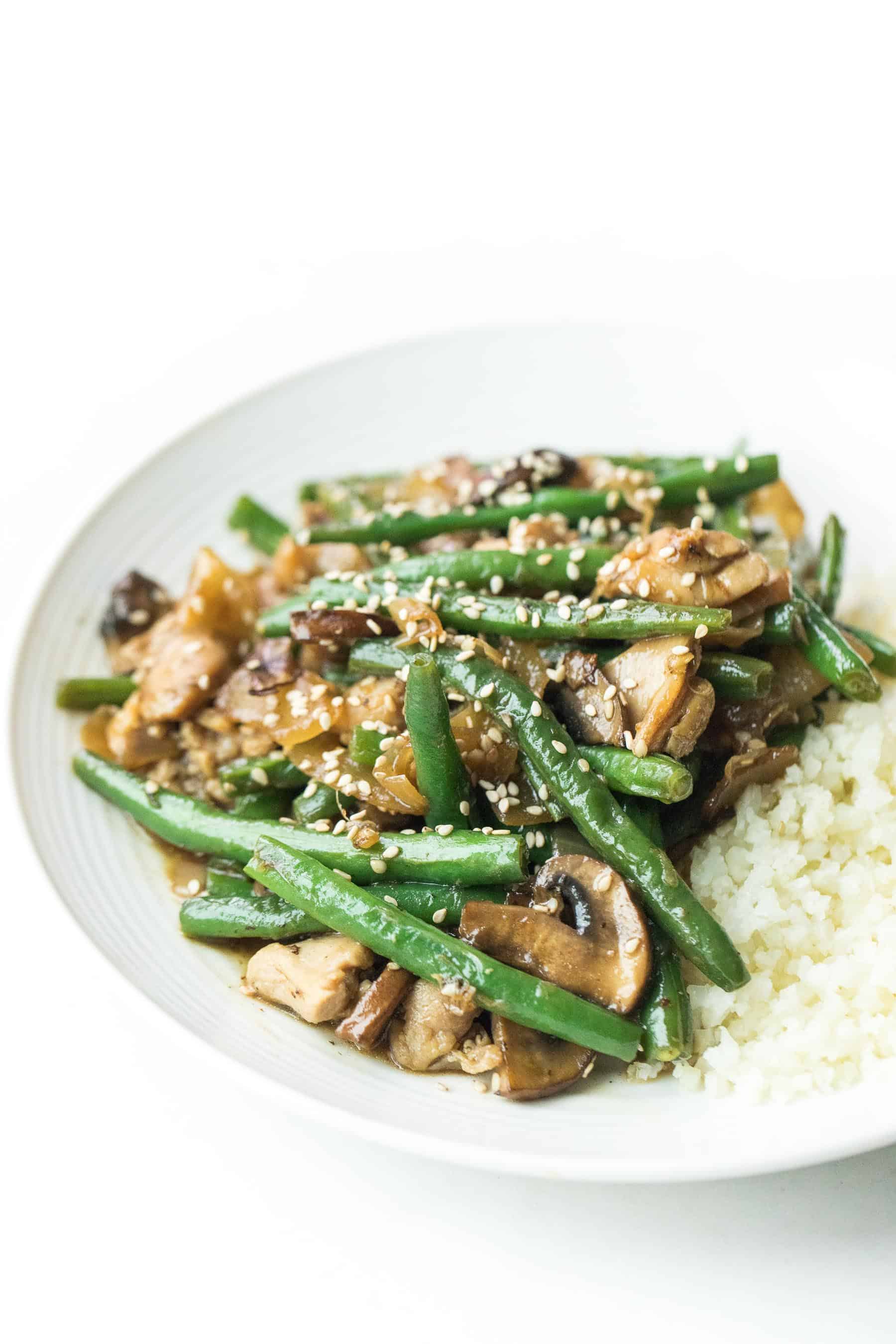 sesame chicken green bean stir fry on a white plate with cauliflower rice