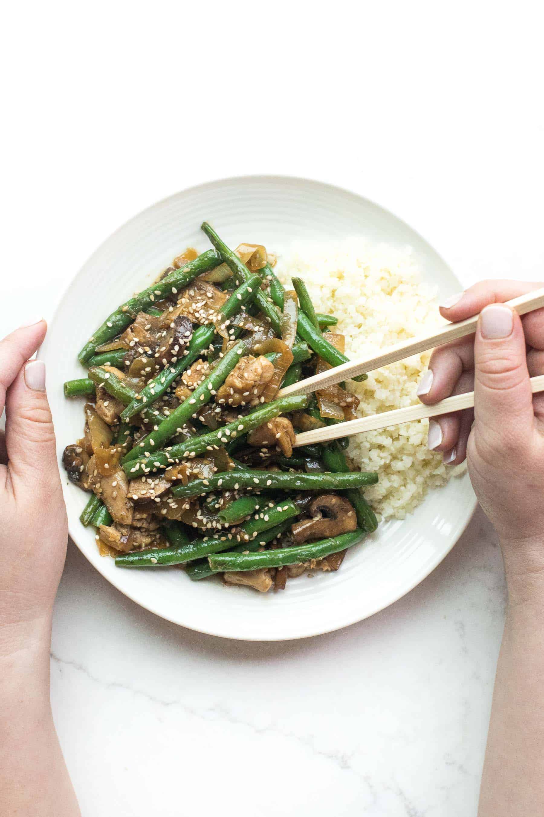 2 hands holding chopsticks to eat sesame chicken green bean stir fry