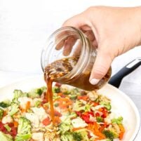 Pouring thick, glossy stir fry sauce over cooked chicken and vegetables in a white skillet, showing texture and consistency.
