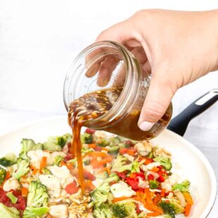Pouring thick, glossy stir fry sauce over cooked chicken and vegetables in a white skillet, showing texture and consistency.