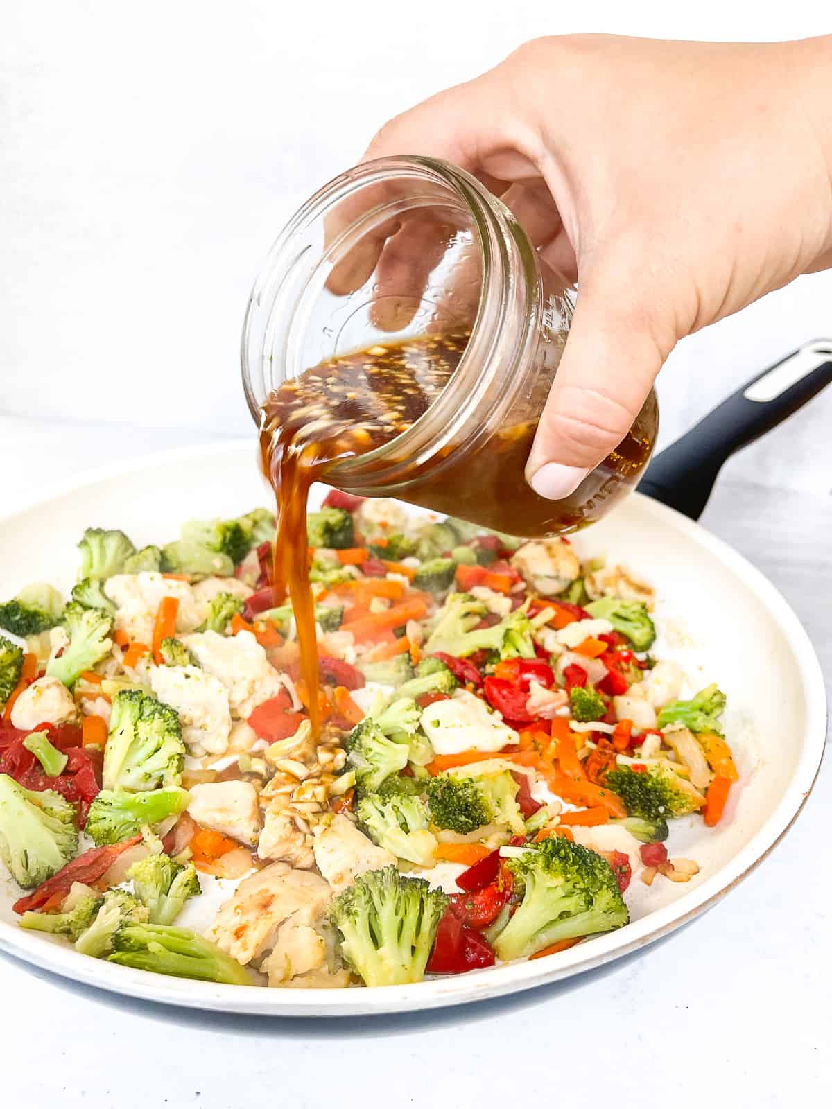 a hand pouring the best sauce over stir fried chicken and vegetables