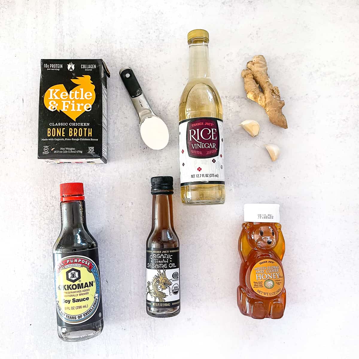 Ingredients for stir fry sauce laid out on a white surface: broth, soy sauce, sesame oil, and fresh garlic and ginger.
