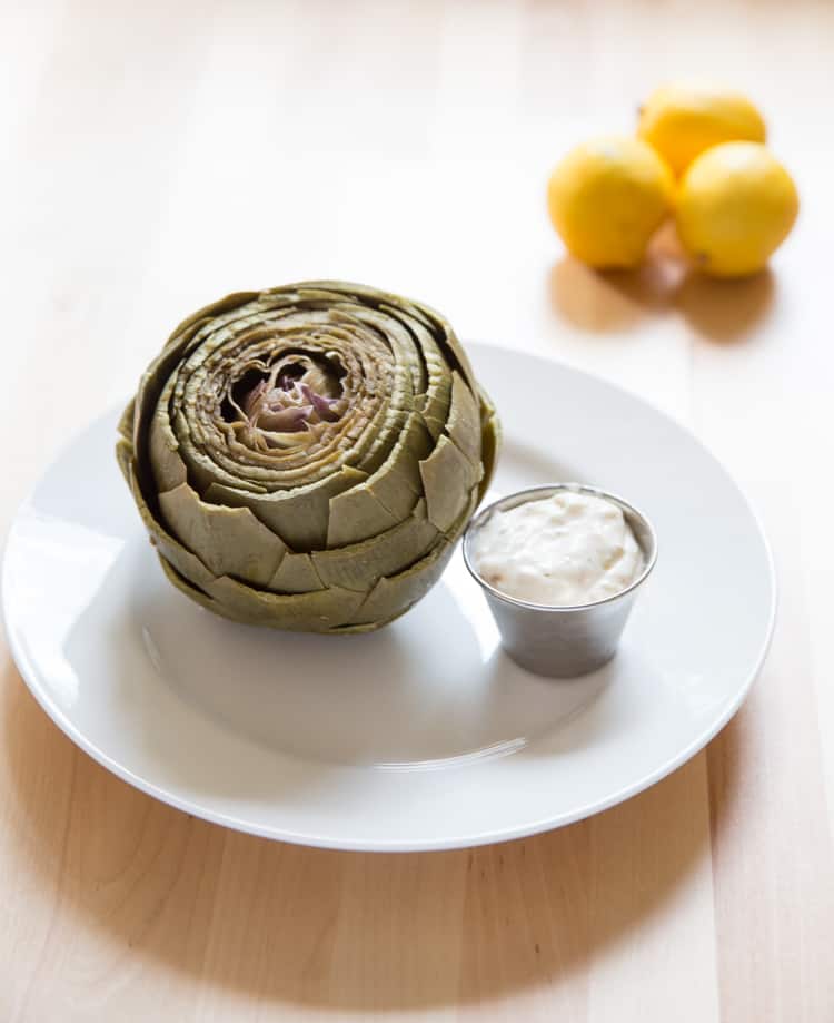 close up of pressure cooker artichokes with artichoke dipping sauce on a white plate.