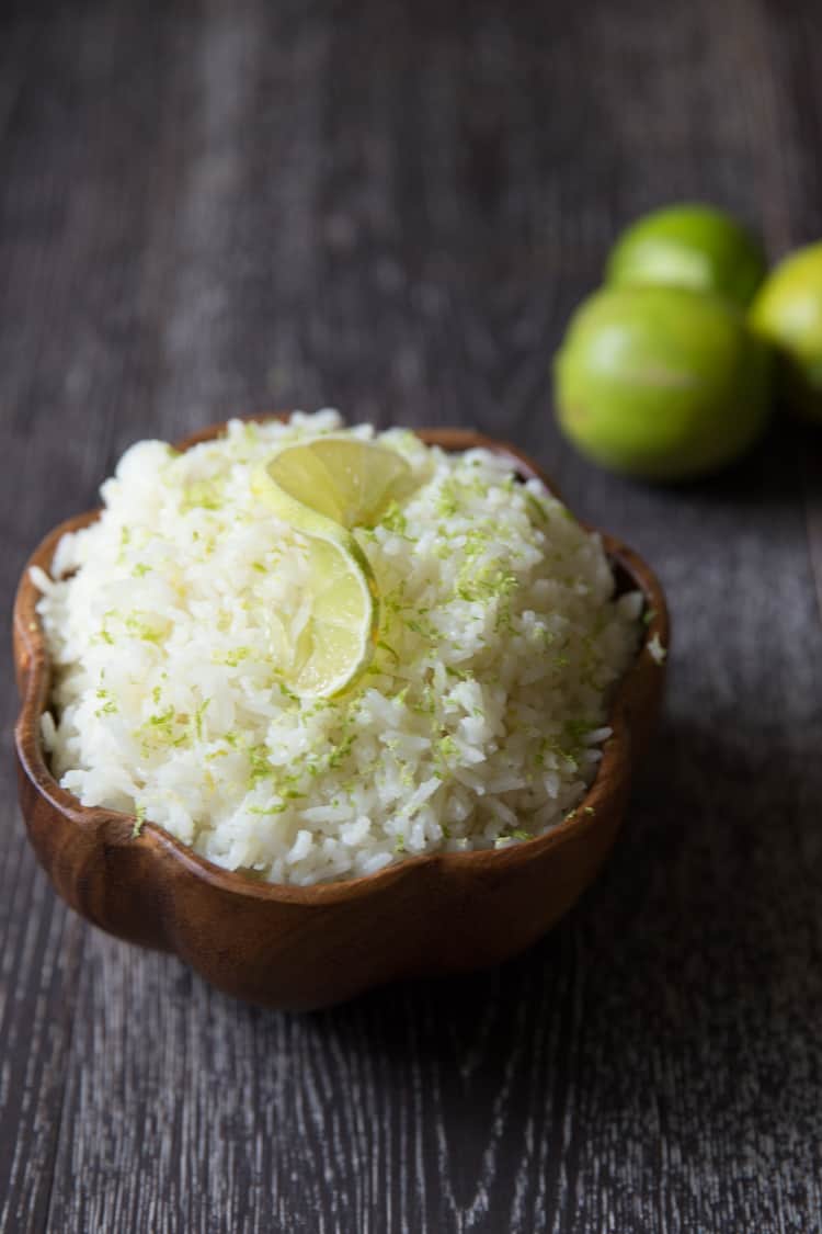 a bowl filled with coconut jasmine rice and topped with a lime wedge and lime zest.