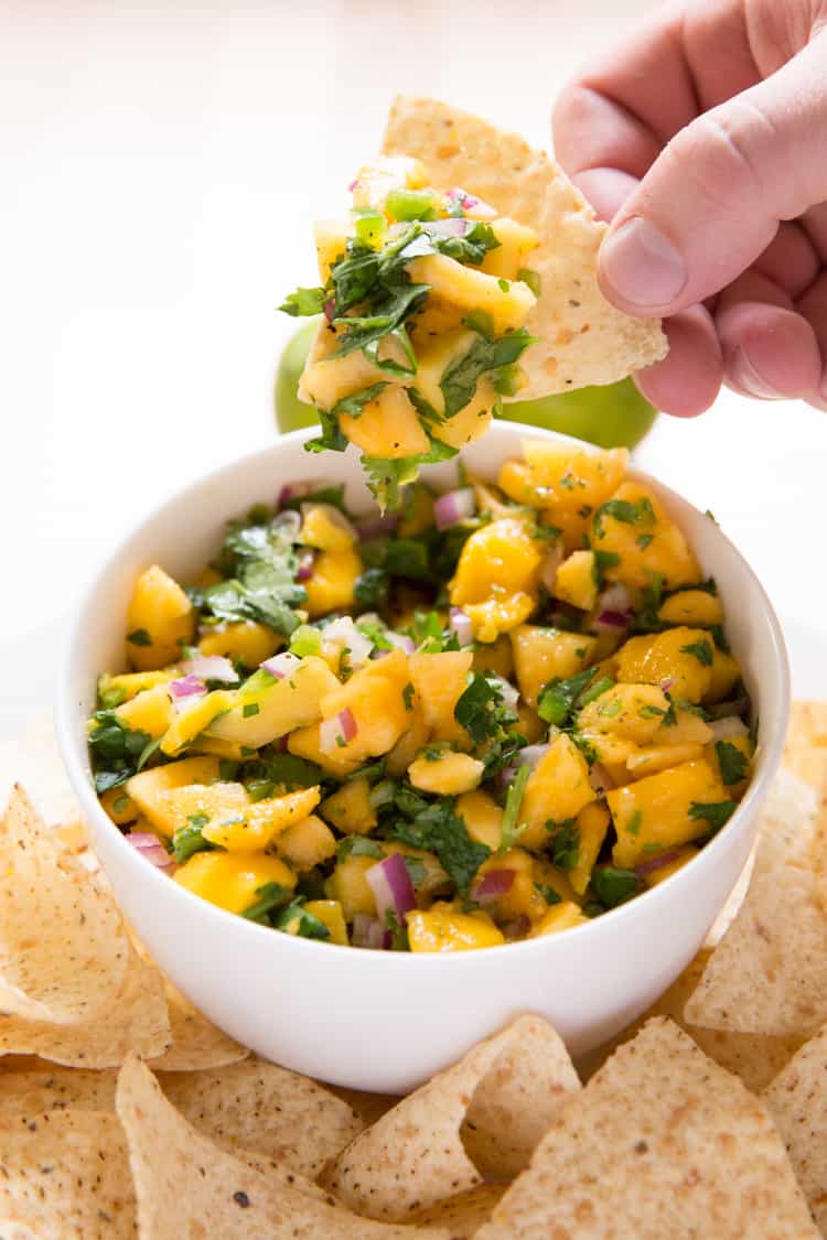 a hand holding a chip topped with mango papaya salsa