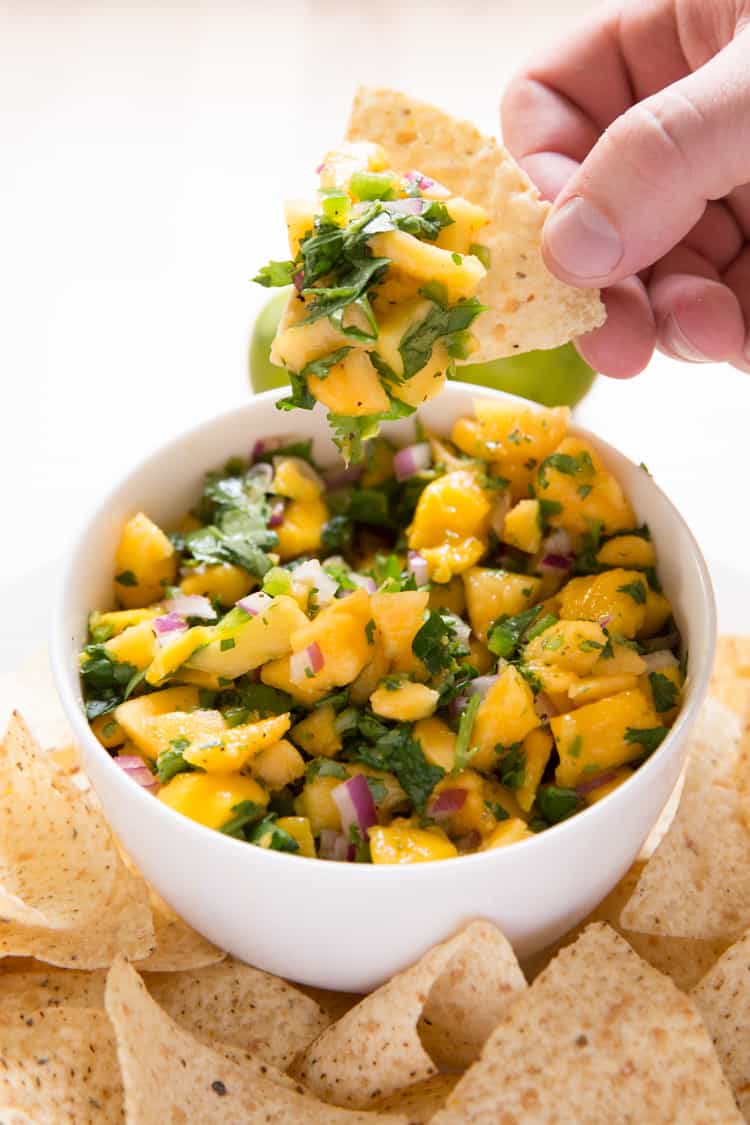 a hand holding a chip topped with mango papaya salsa