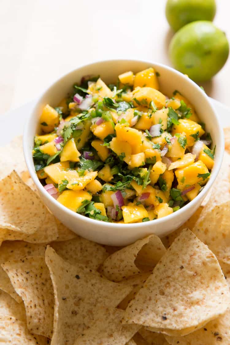 a small white bowl of mango papaya salsa surrounded by tortilla chips