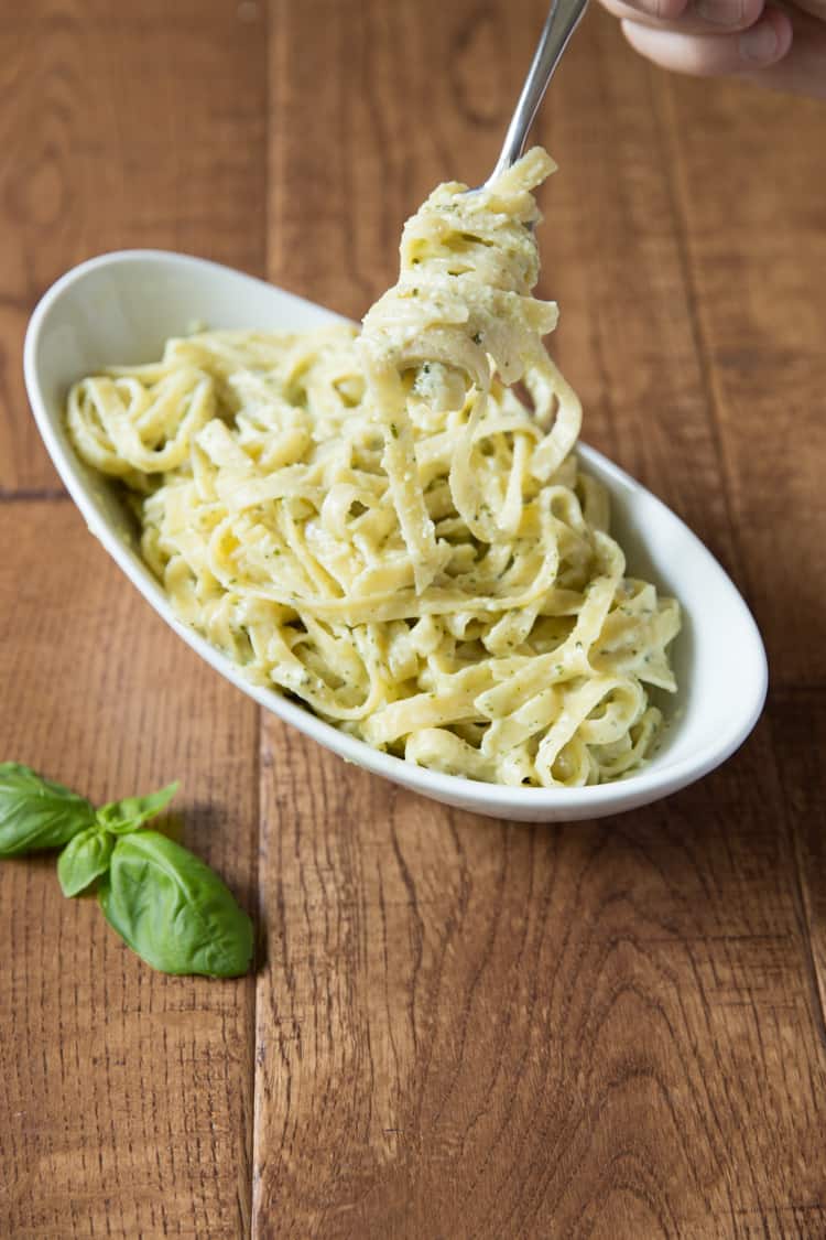 creamy pesto pasta in a white bowl with pasta swirled around a fork