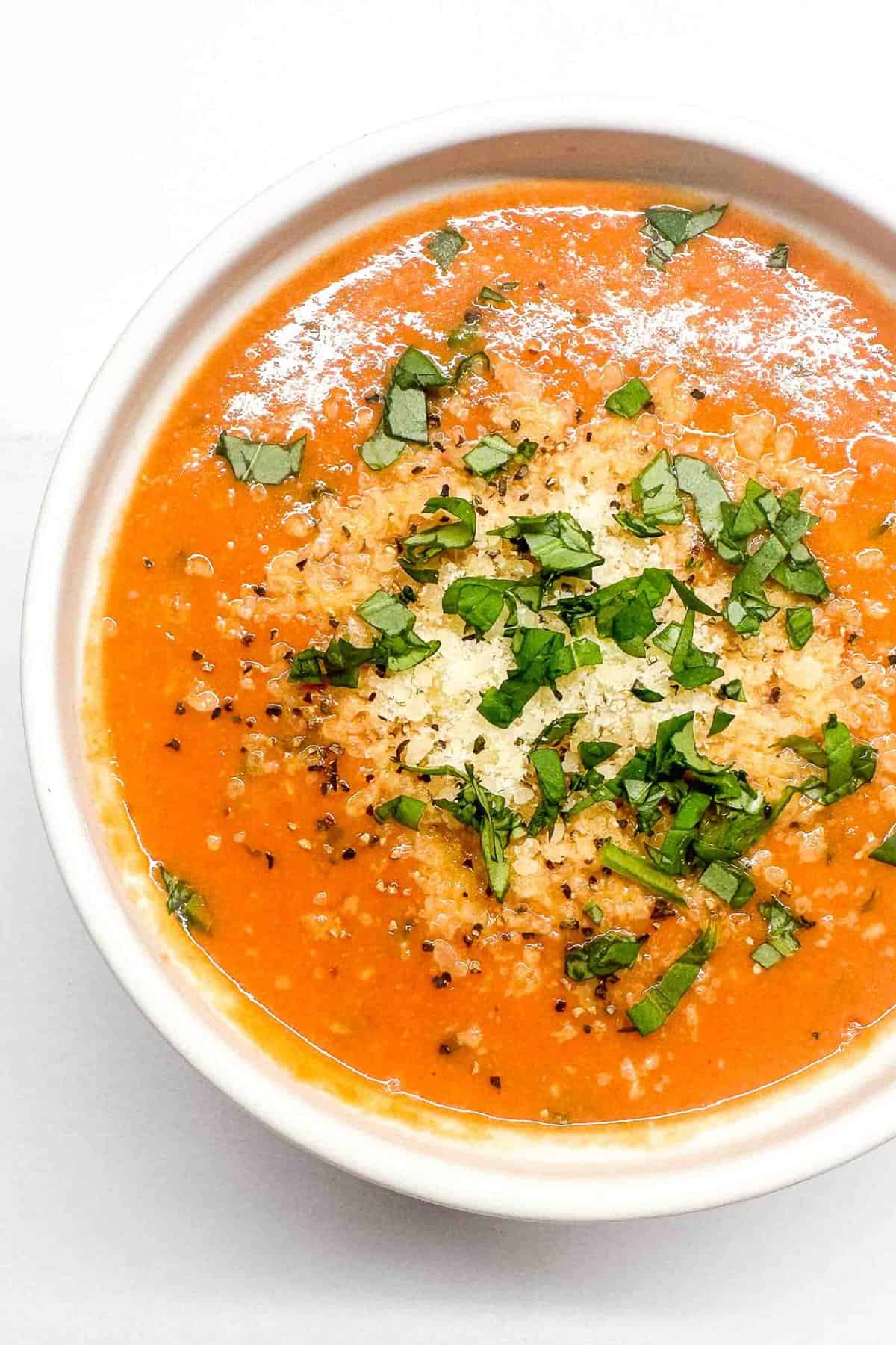an overhead shot of creamy tomato basil soup topped with fresh parmesan and chopped basil