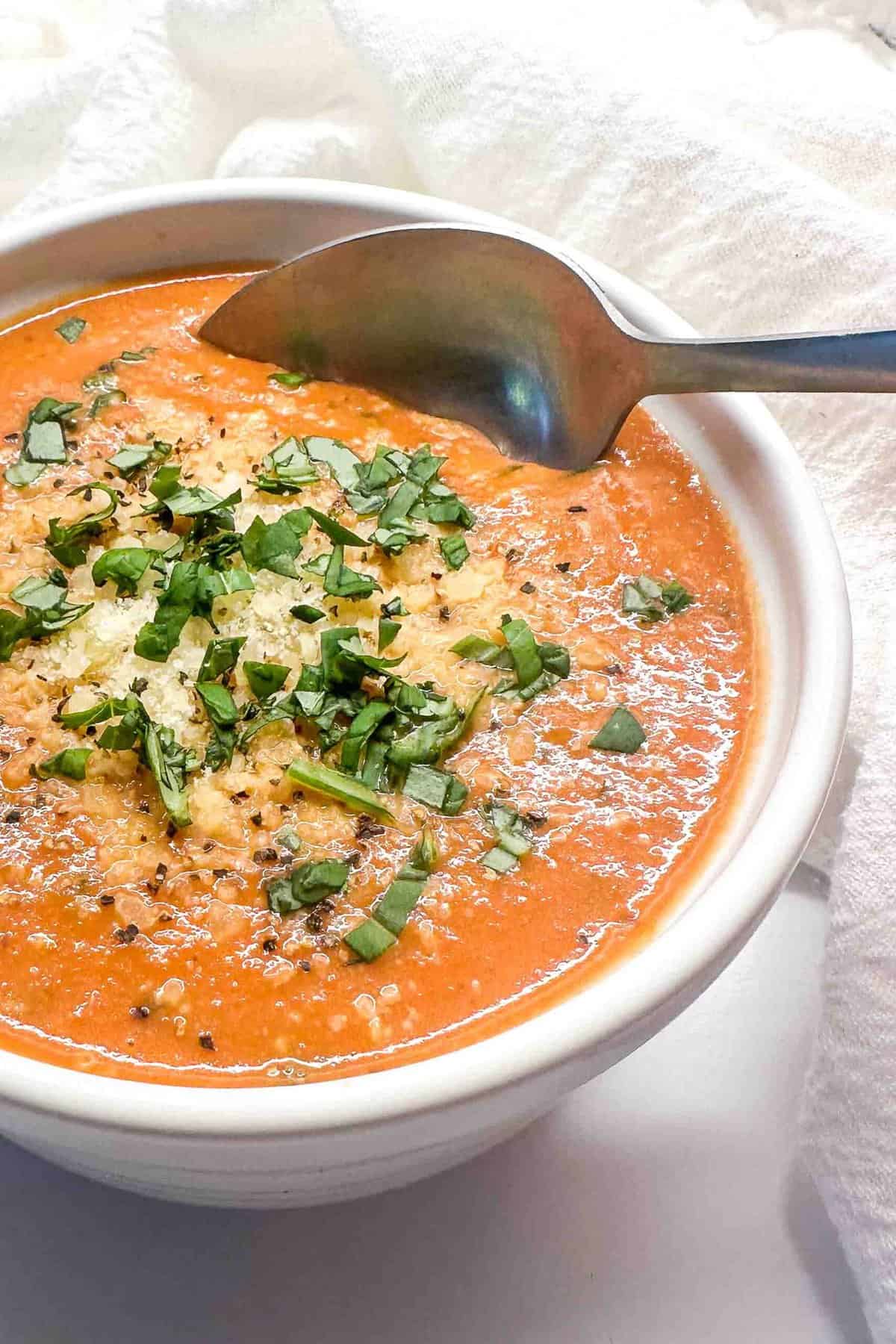a spoon scooping creamy tomato basil soup out of a white bowl
