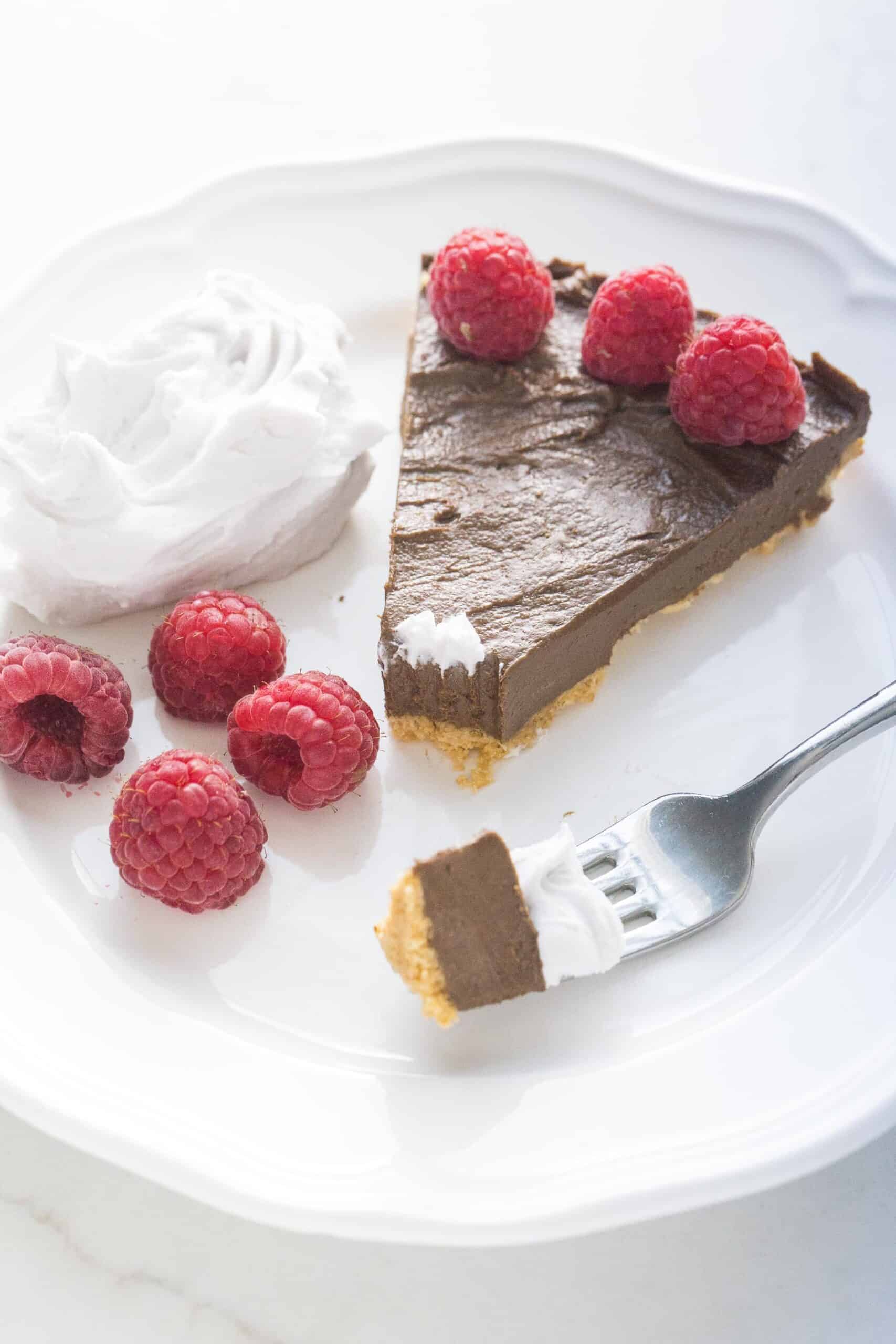 fork taking a bite out of healthy chocolate tart with raspberries and coconut whipped cream