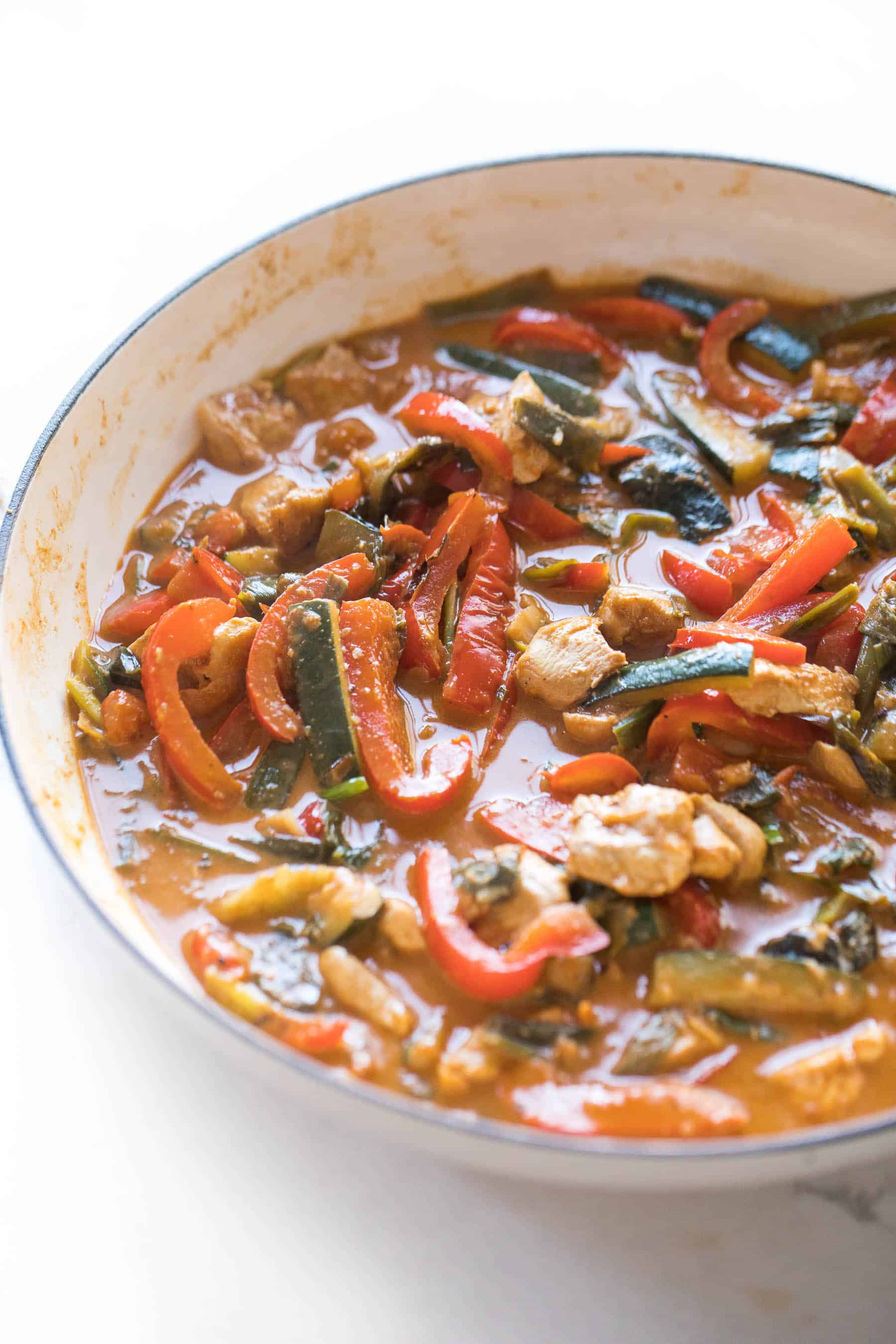 thai red curry with chicken and vegetables in a white skillet