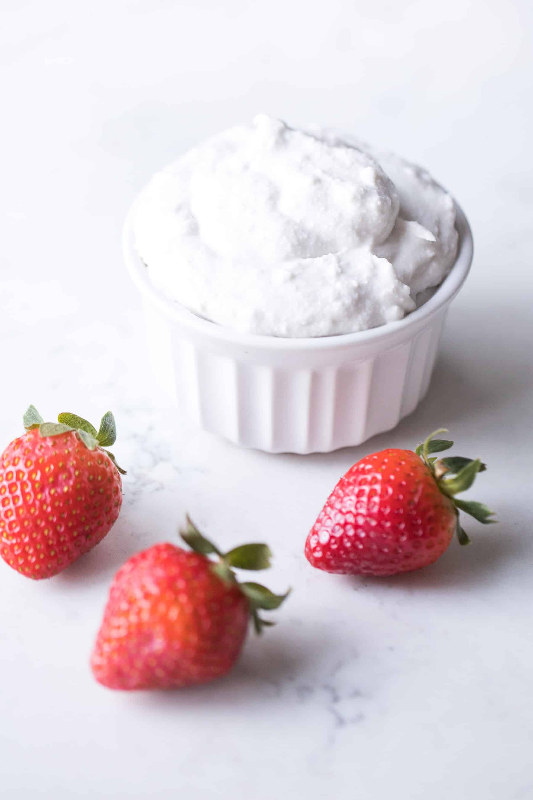 a white bowl of coconut whipped cream with strawberries in the background