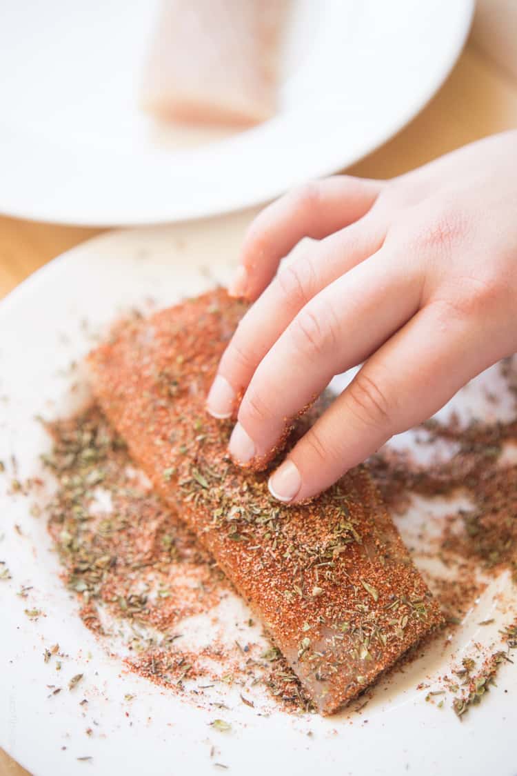 a hand dredging a mahi mahi filet in cajun dry rub