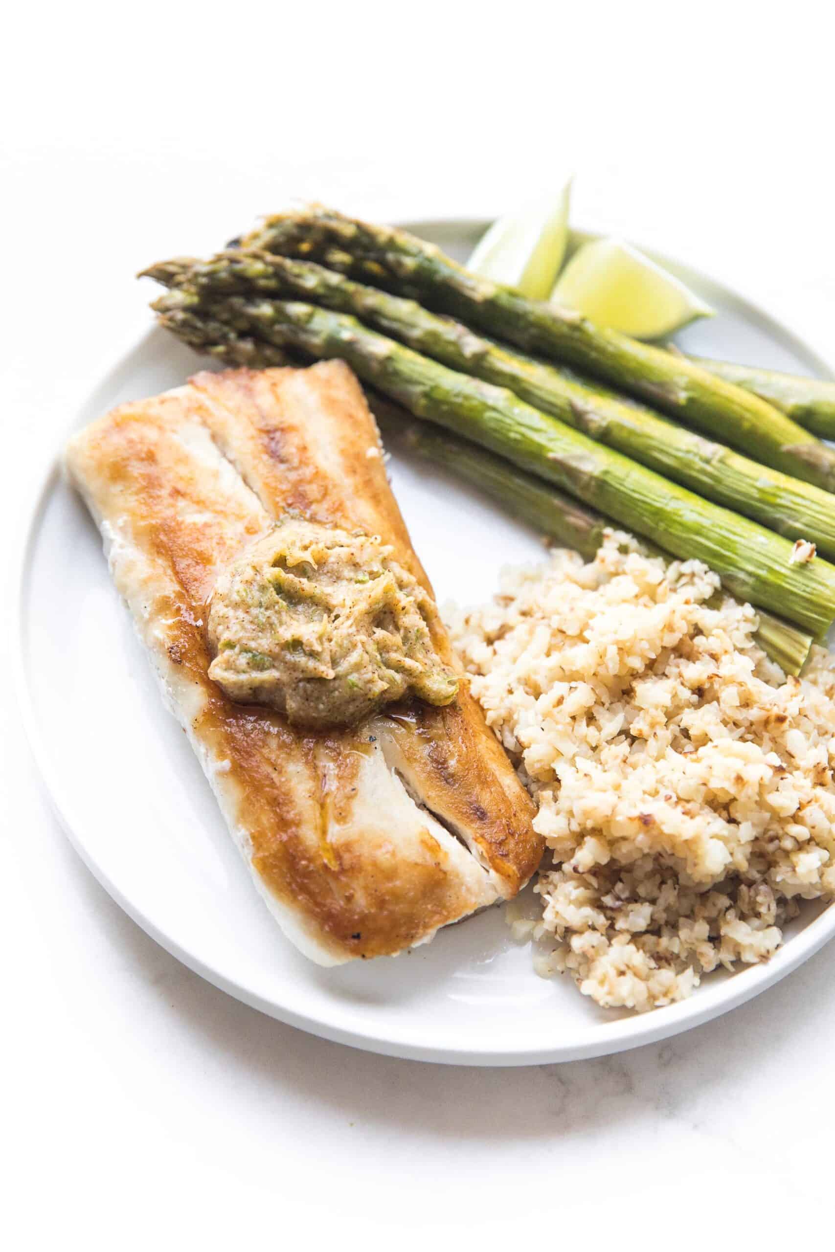 MAHI MAHI WITH CHILI LIME COMPOUND BUTTER WITH CAULIFLOWER RICE AND ASPARAGUS ON A WHITE PLATE AND BACKGROUND