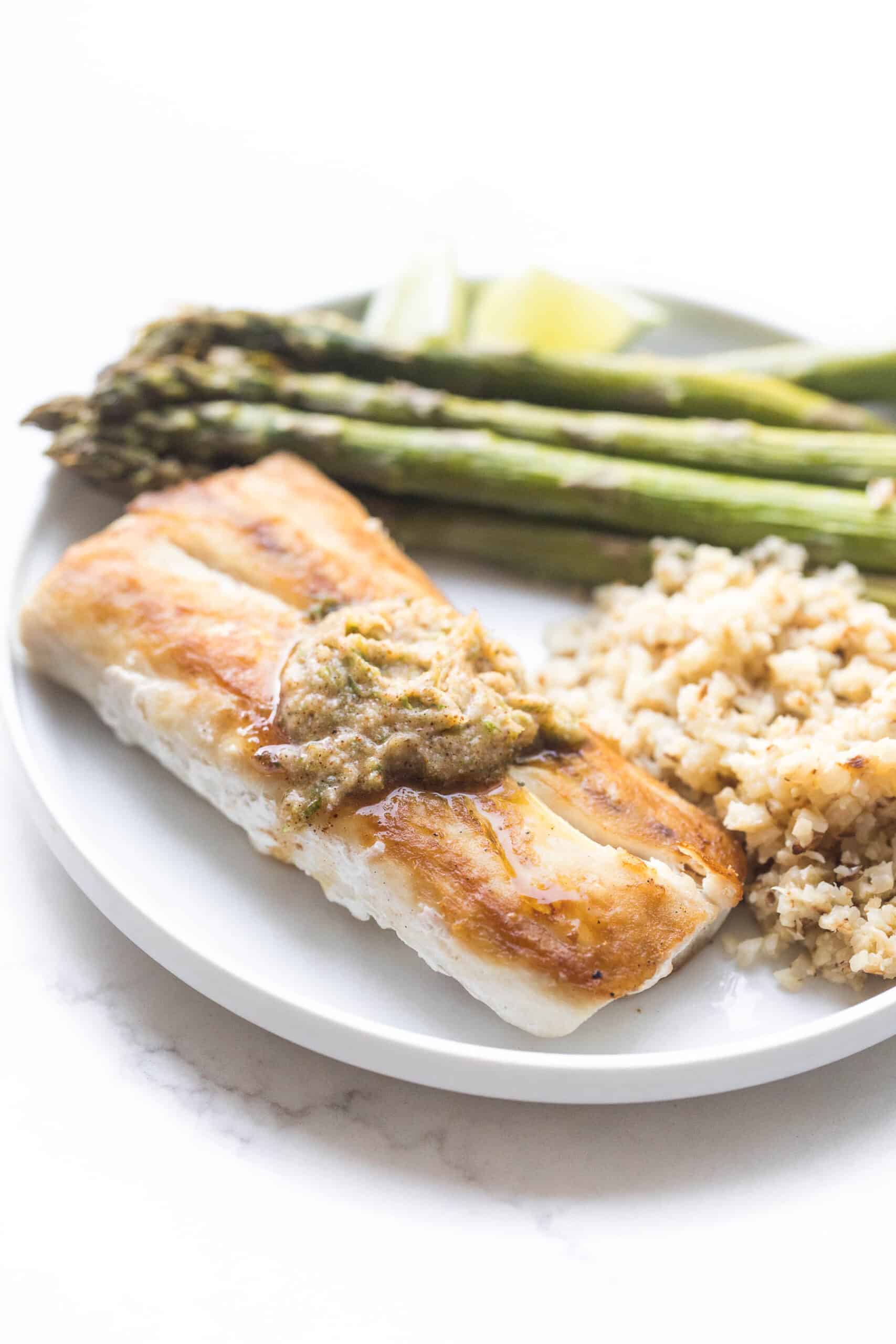 MAHI MAHI WITH CHILI LIME COMPOUND BUTTER WITH CAULIFLOWER RICE AND ASPARAGUS ON A WHITE PLATE AND BACKGROUND