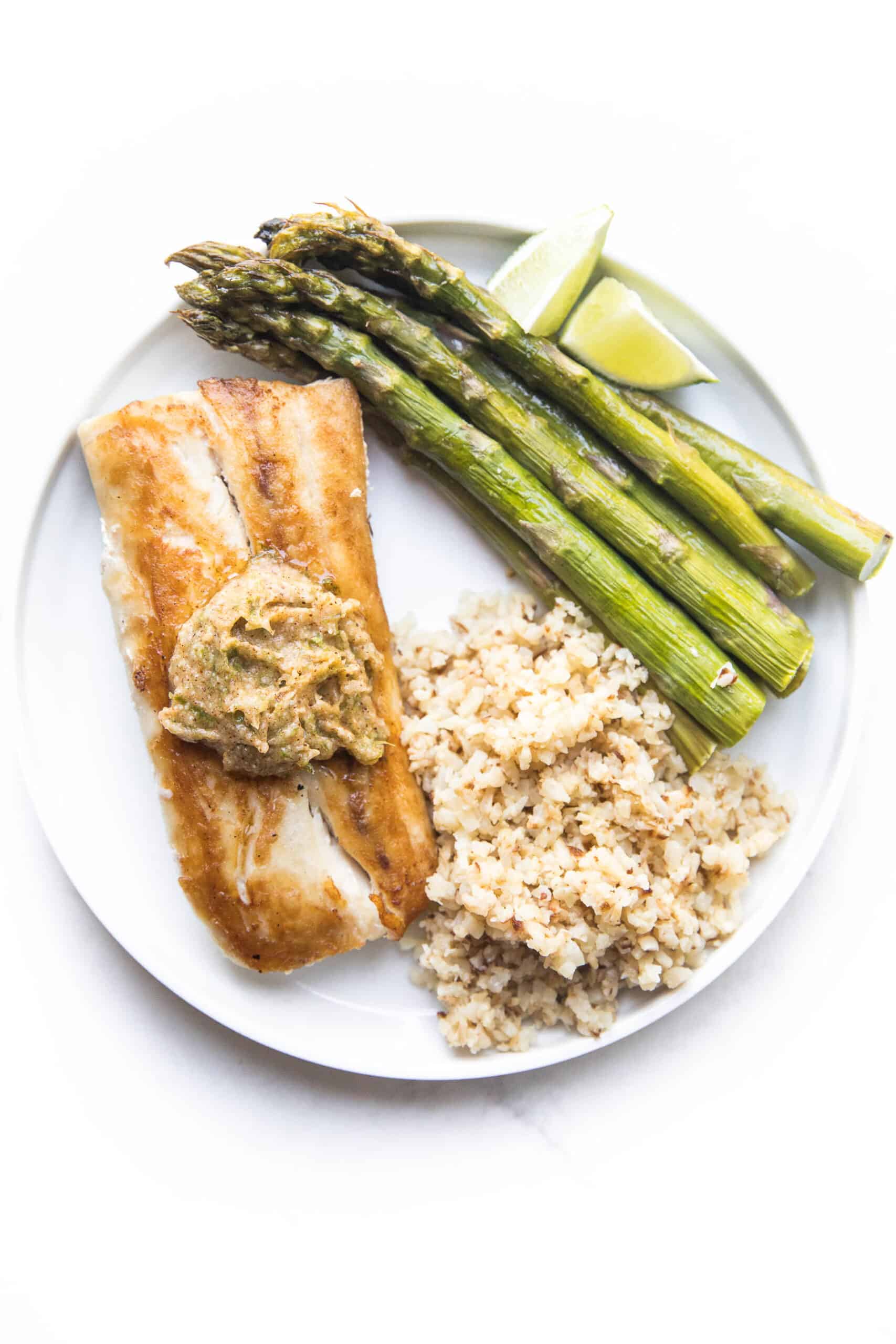 MAHI MAHI WITH CHILI LIME COMPOUND BUTTER WITH CAULIFLOWER RICE AND ASPARAGUS ON A WHITE PLATE AND BACKGROUND