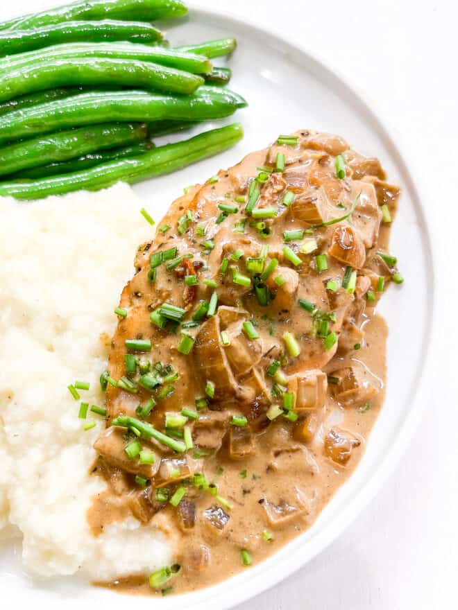 chicken with dijon mustard sauce on a white plate with green beans and mashed potatoes