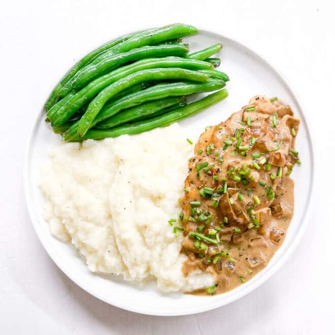chicken with mustard sauce on a white plate with green beans and mashed potatoes
