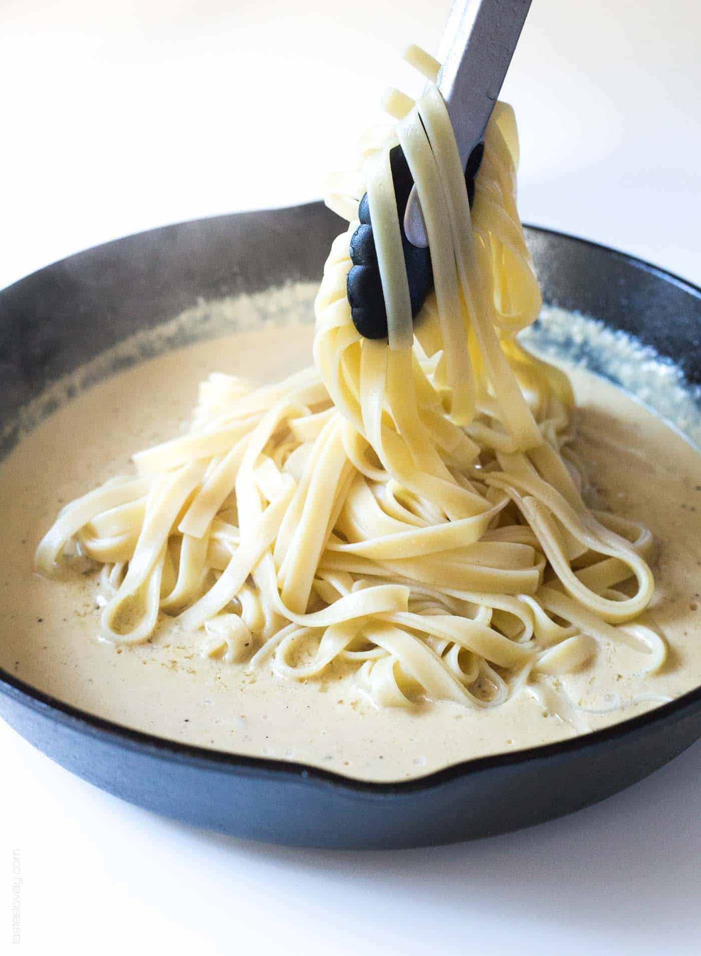 Noodles being dipped in homemade alfredo sauce in a cast iron skillet
