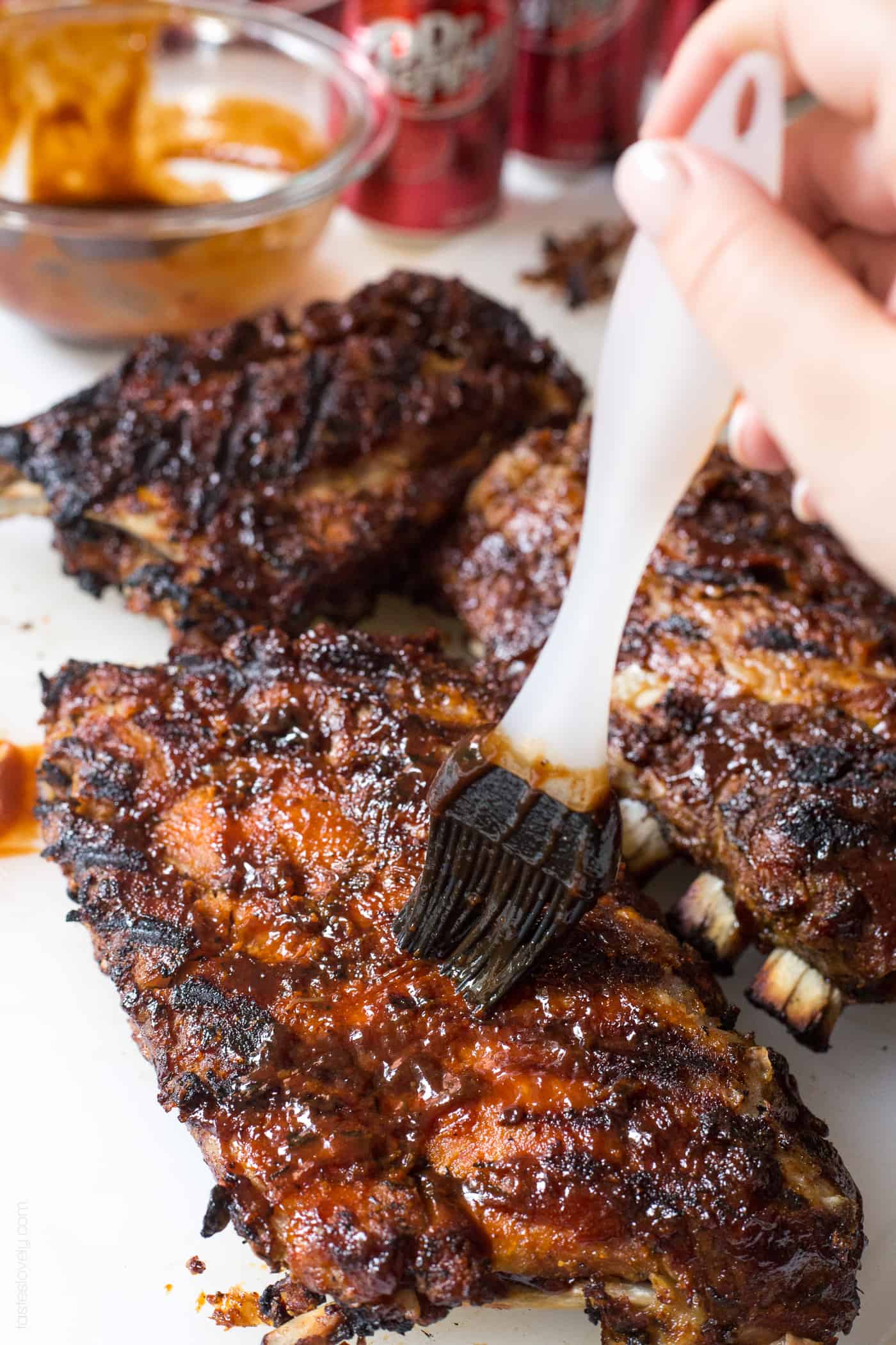 a hand brushing bbq sauce onto ribs