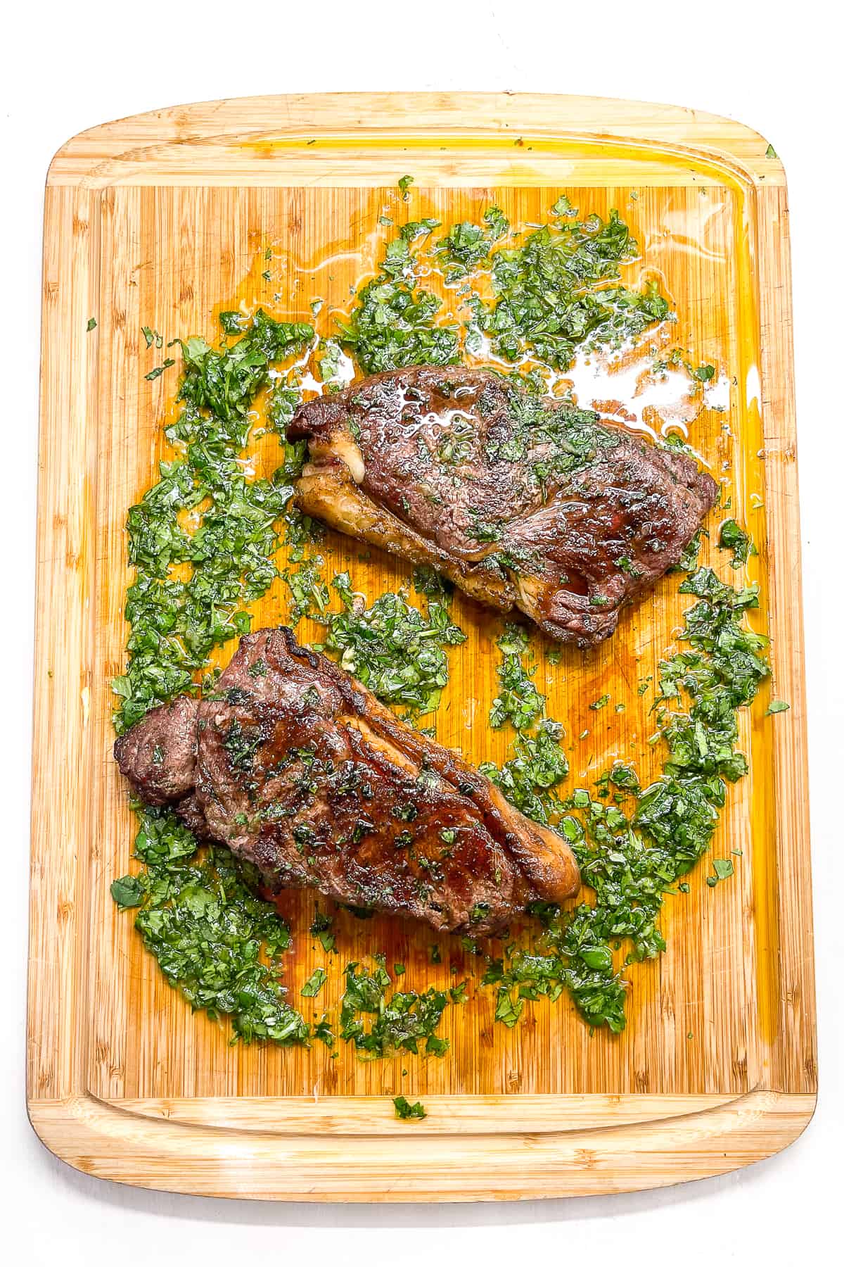 and overhead view of two ny striploin steaks on a cutting board with cilantro garlic sauce