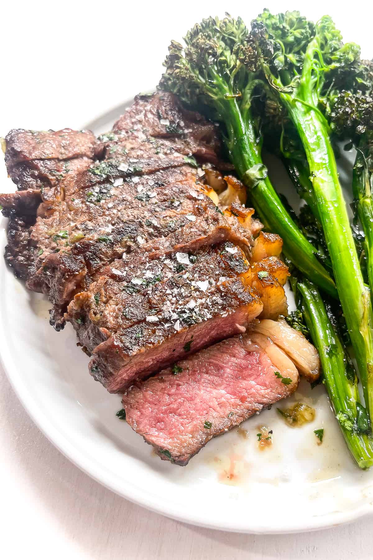 a close up of striploin steak sliced on a white plate with broccolini