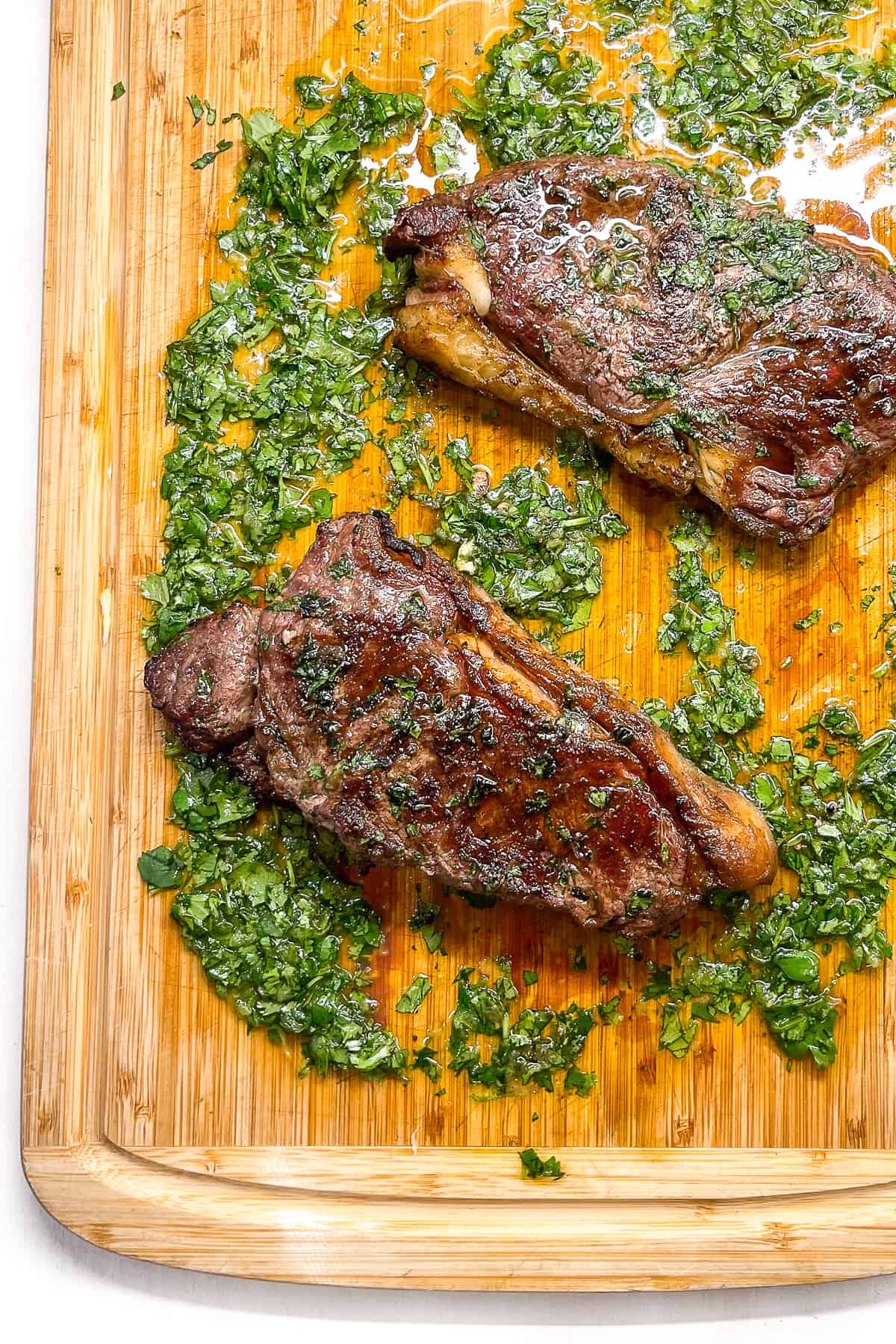 two ny striploin steaks on a cutting board with cilantro garlic sauce