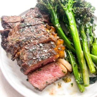 a close up of steak sliced on a white plate with broccolini