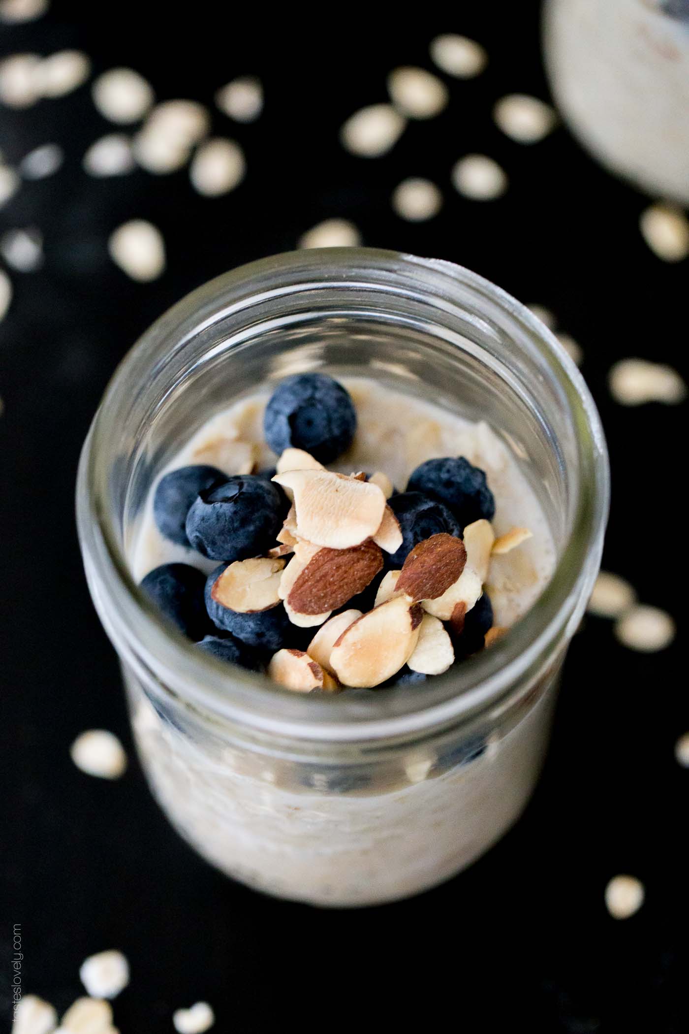 an overhead shot of overnight oats with protein powder in a glass jar and topped with blueberries and toasted almonds