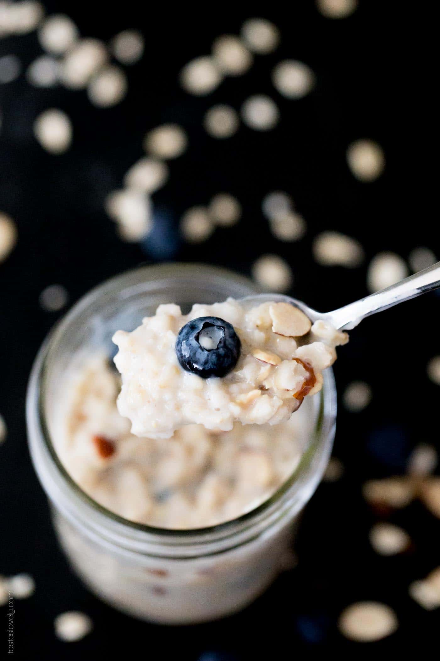 a closeup photo of a silver spoon with holding blueberry overnight oats over a glass jar