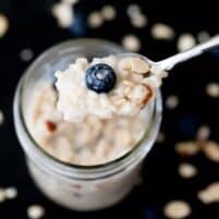 a closeup photo of a silver spoon with holding blueberry overnight oats over a glass jar