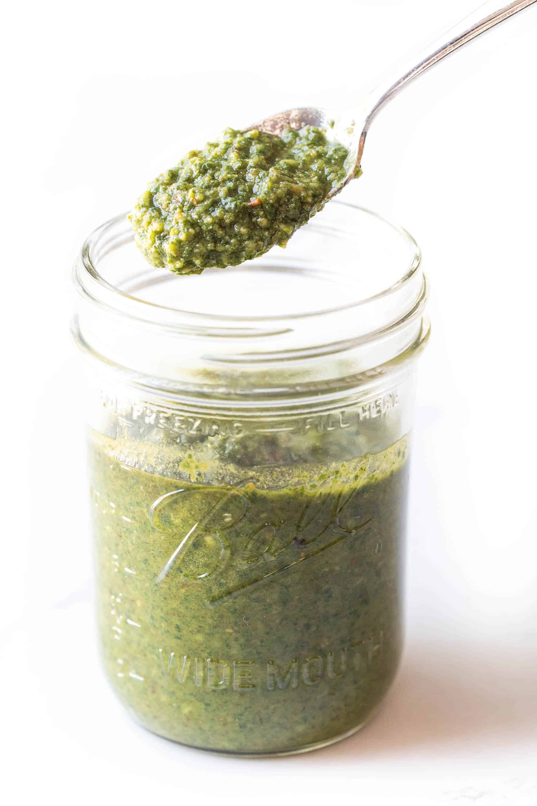 Spoon holding pesto in a mason jar on a white background