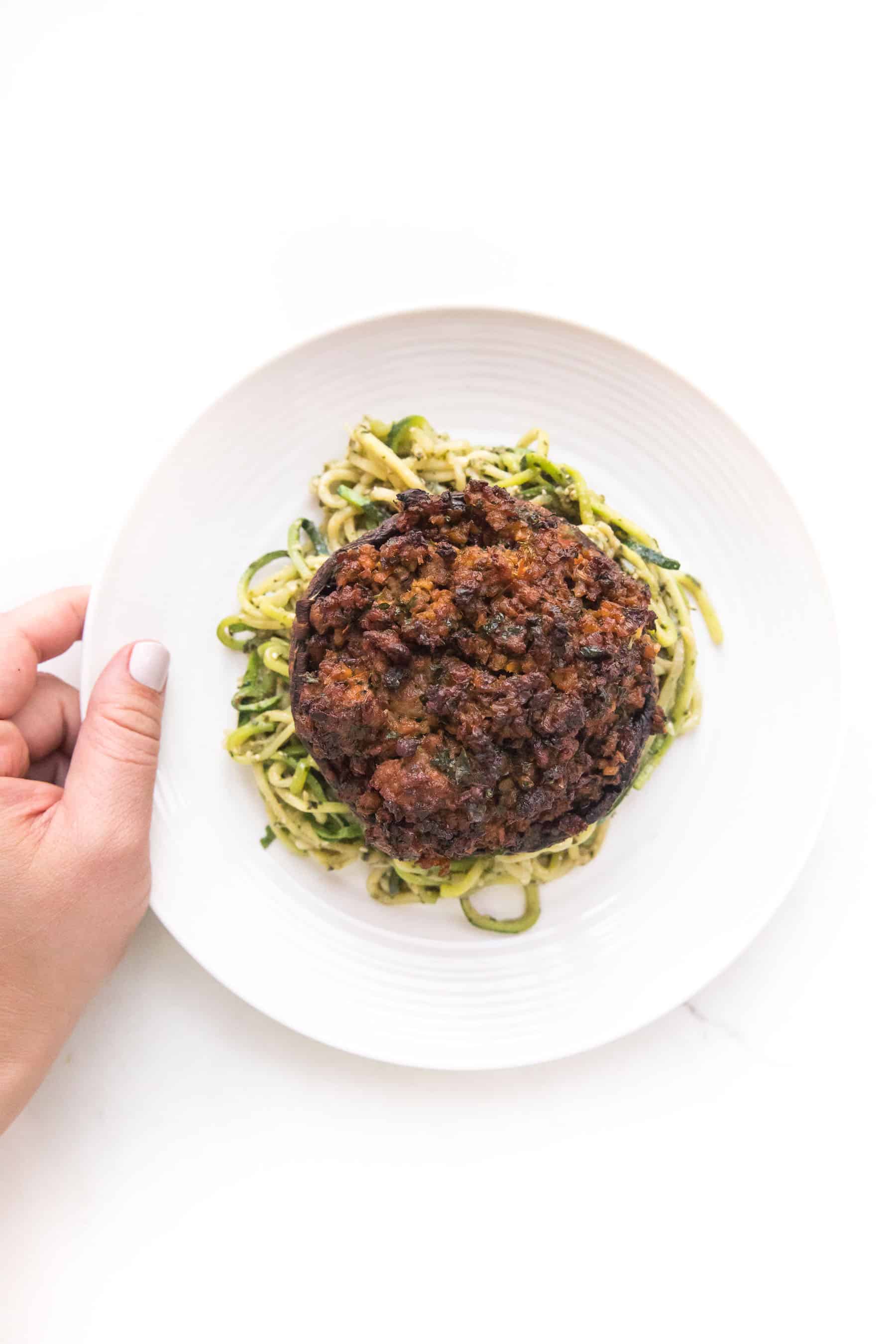 close up of sausage stuffed portobello mushrooms over zucchini noodles on a white plate