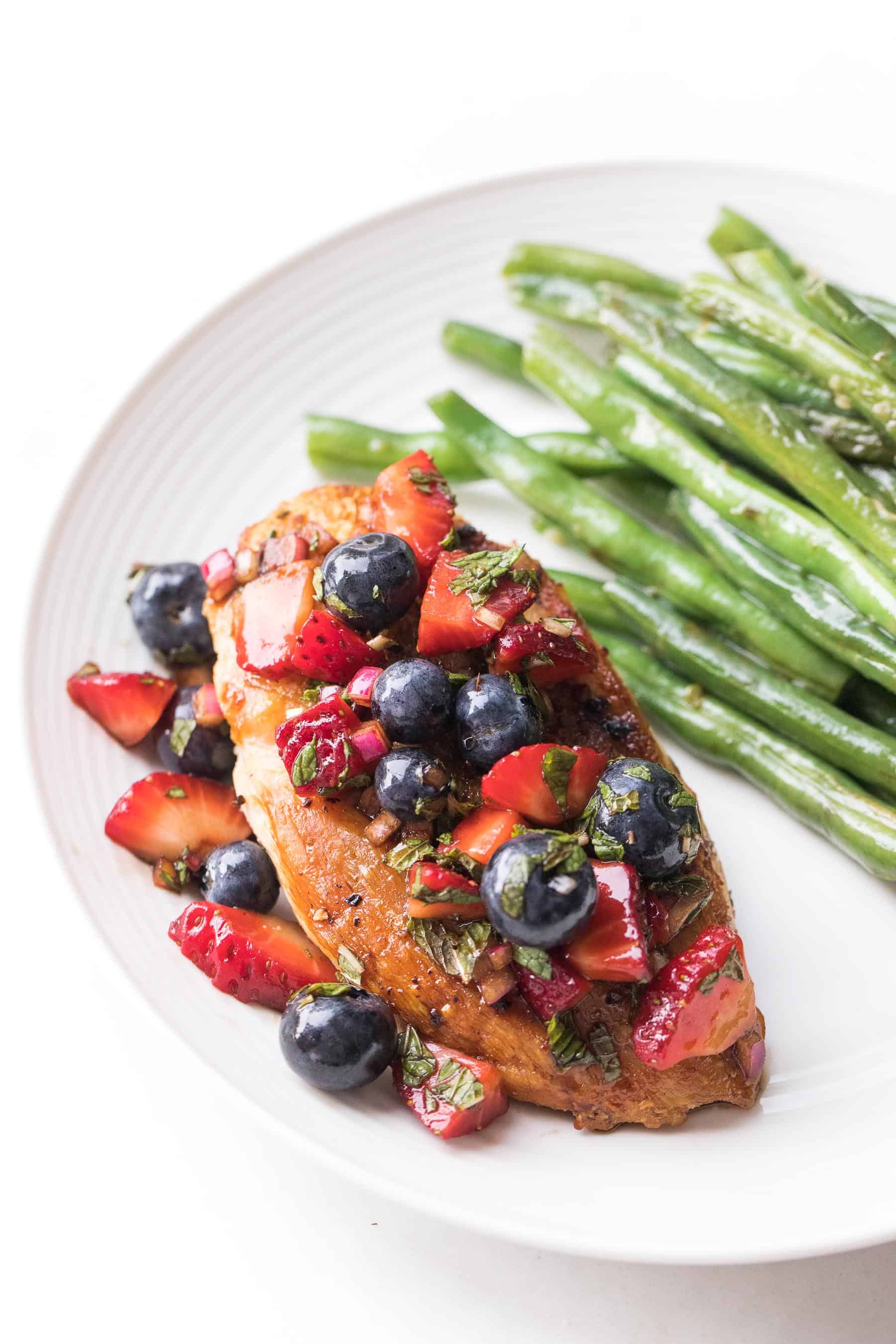 chicken topped with blueberry and strawberry salsa on a white plate and a white background